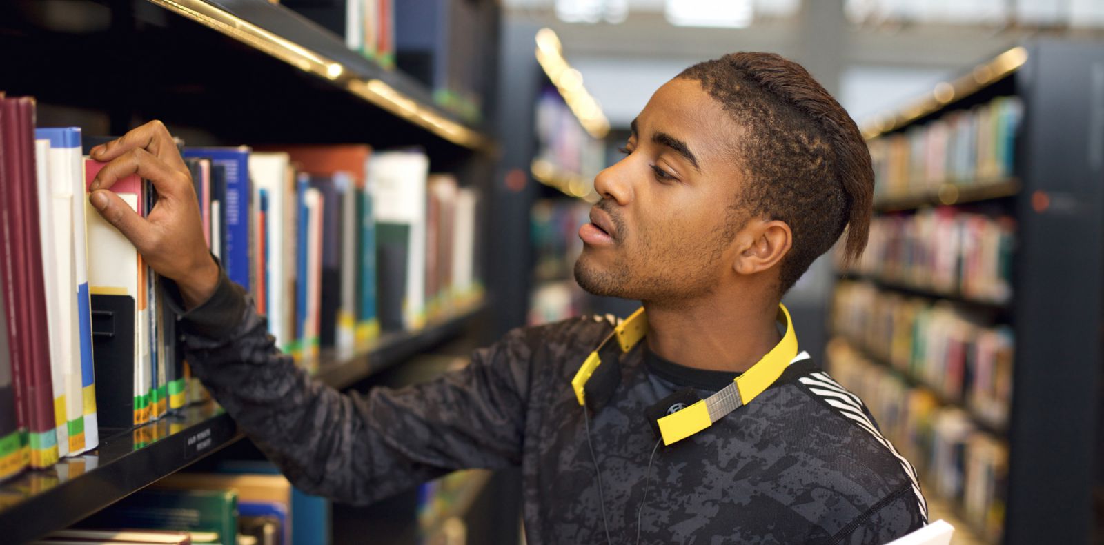Student pulling book off shelf in library