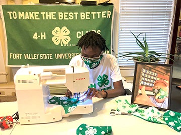 Fort Valley State University 4-H’er Janya Green, sews 4-H masks for essential workers at her home in Sylvester, Georgia. In the portrait on the table is Gary Black, Georgia Commissioner of Agriculture, wearing the first 4-H mask Janya made. The mask is named the 4-H Janya Green Mask for All. (Photo courtesy of Linda Green)