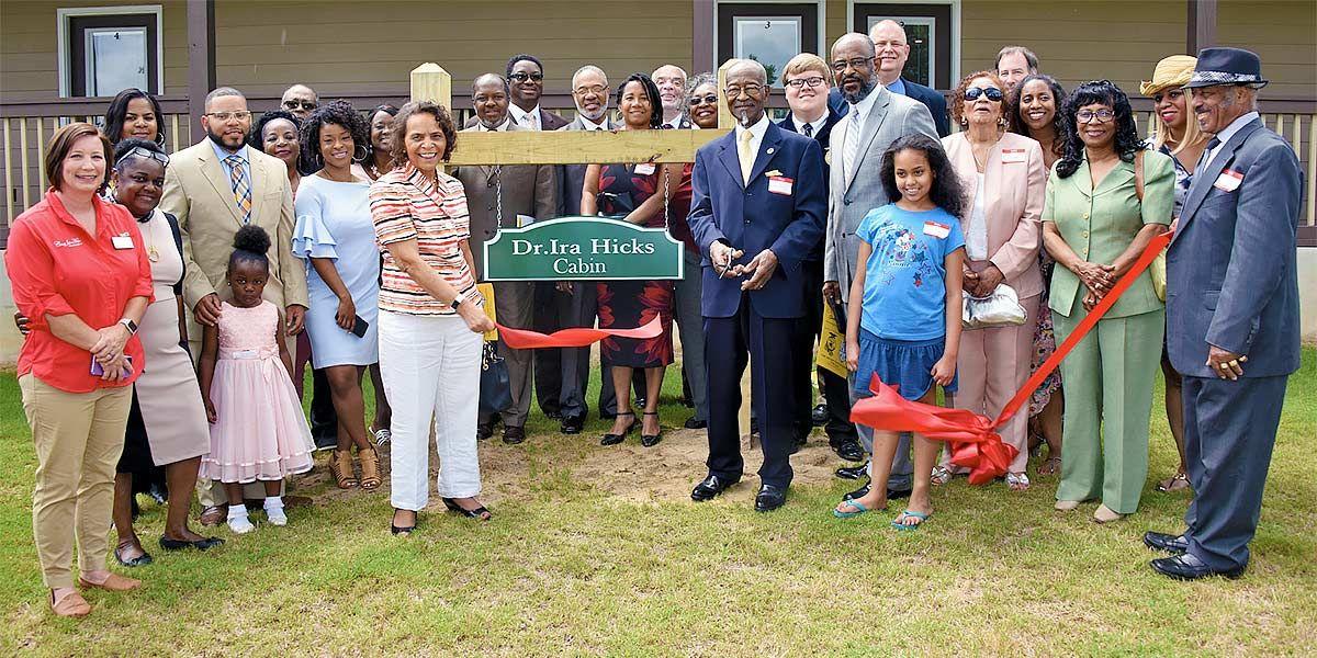 Dr. Ira Hicks (center right) is joined by family, friends, Camp John Hope officials and others as he cuts a ceremonial ribbon opening a cabin named in his honor at Camp John Hope on May 22.