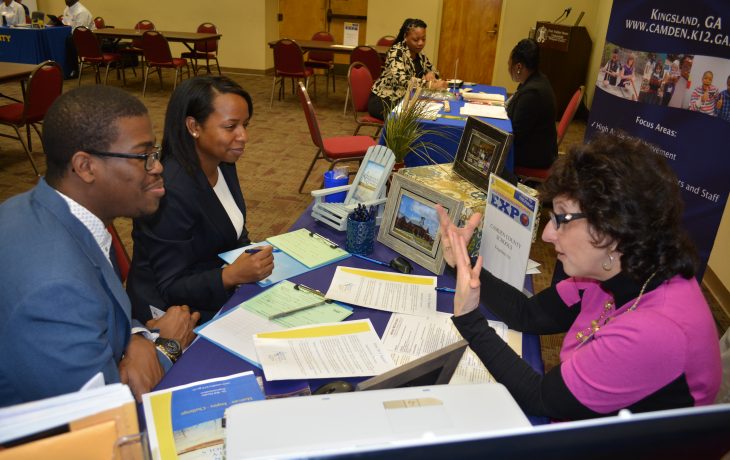 Two student seated at table speaking with recruiter at career expo