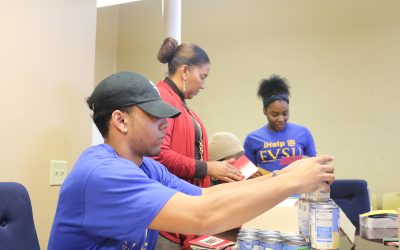 A volunteer works with students to prepare holiday cards and canned foods to deliver to the military, nursing home residents, and the local community.