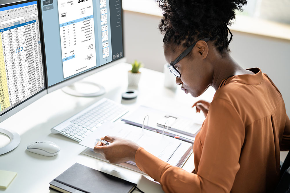 Woman at desk with computer displaying spreadsheets