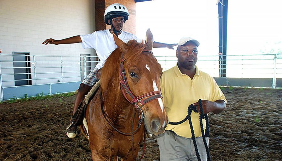 Person riding a horse with his arms out while another person guides horse.