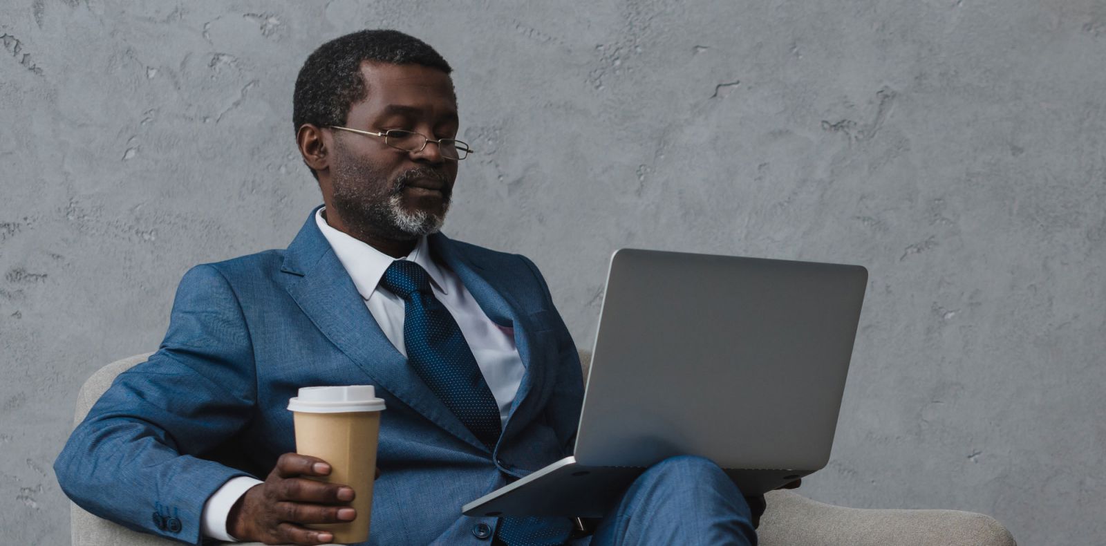 Mature man seated with laptop holding a coffee