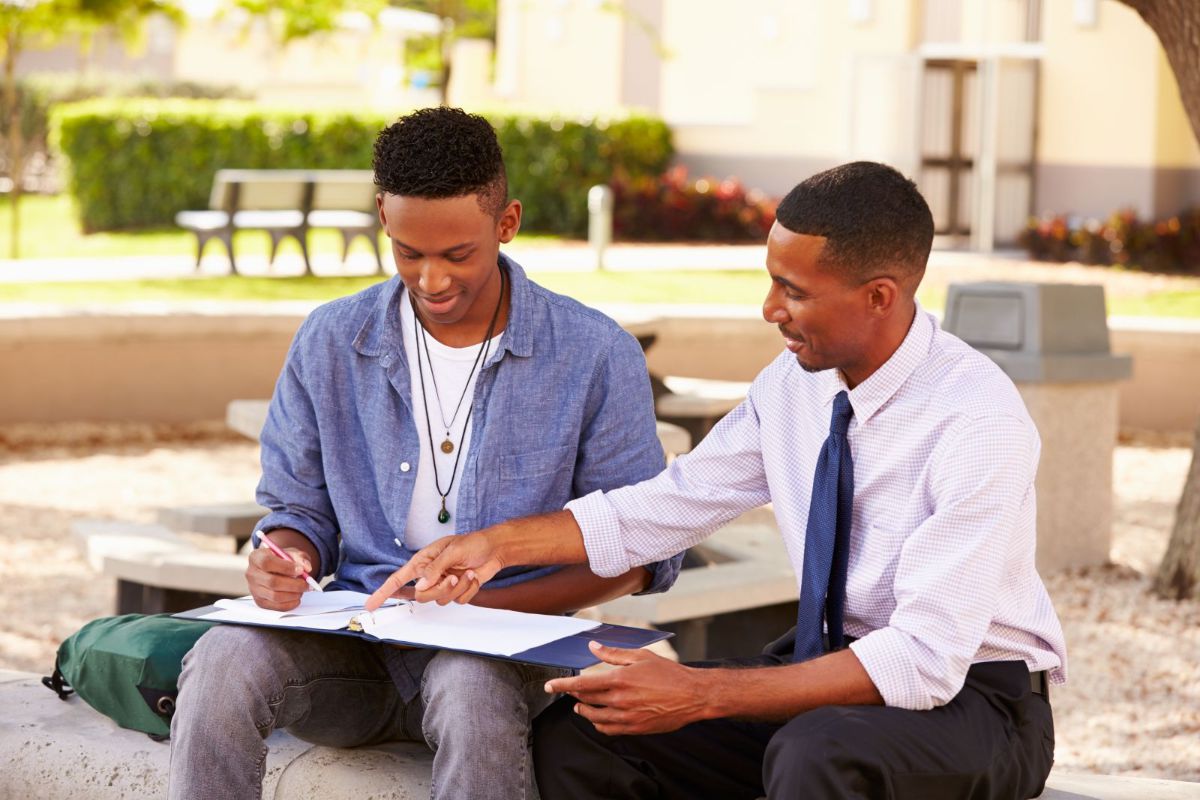 two men seated on outside bench looking at ring binder