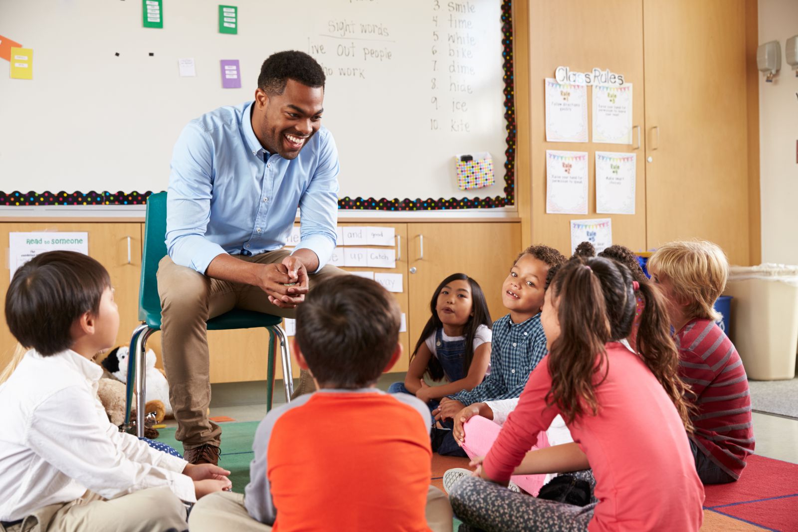 Teacher seated in chair surrounded by young children seated on classroom floor