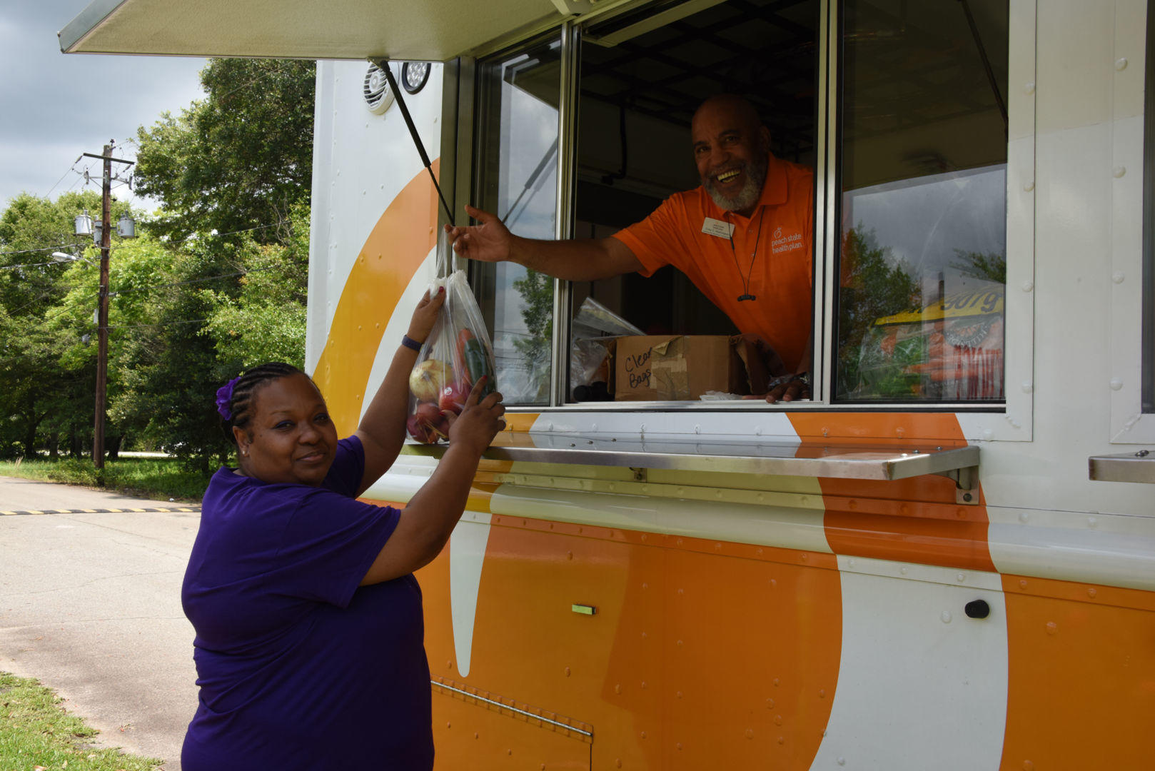 Craig Washington (right), the community coordinator for the Peach State Health Plan, delivers a bag of fresh fruits and vegetables to DeVona Robinson (left) during the Peach State Health Plan’s Mobile Market visit to Fort Valley on May 31.