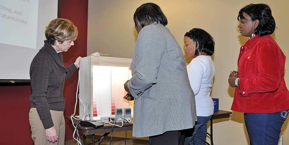 Sarah Kirby (left), housing specialist for North Carolina State University, uses a light demonstration box to show Fort Valley State University extension personnel energy usage with three different types of light bulbs.