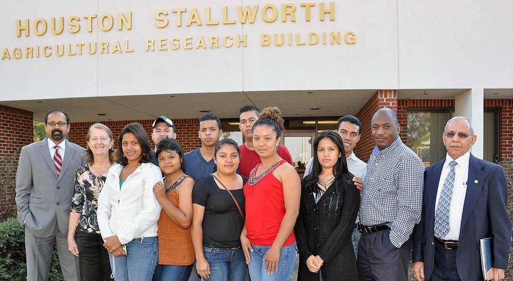 Students visiting from Honduras gather with their professor and Fort Valley State University leaders in front of the Houston Stallworth agricultural research building.