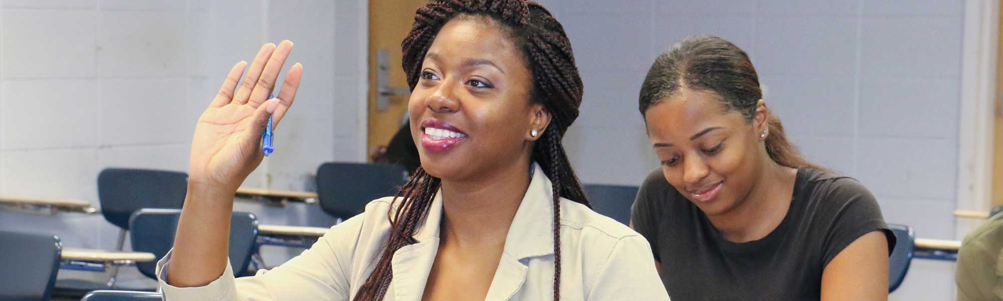 Young woman at classroom desk raising her hand