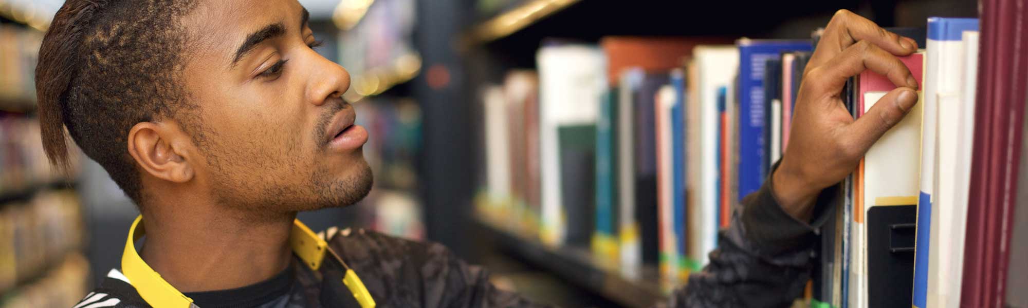 Young man pulling book off library shelf