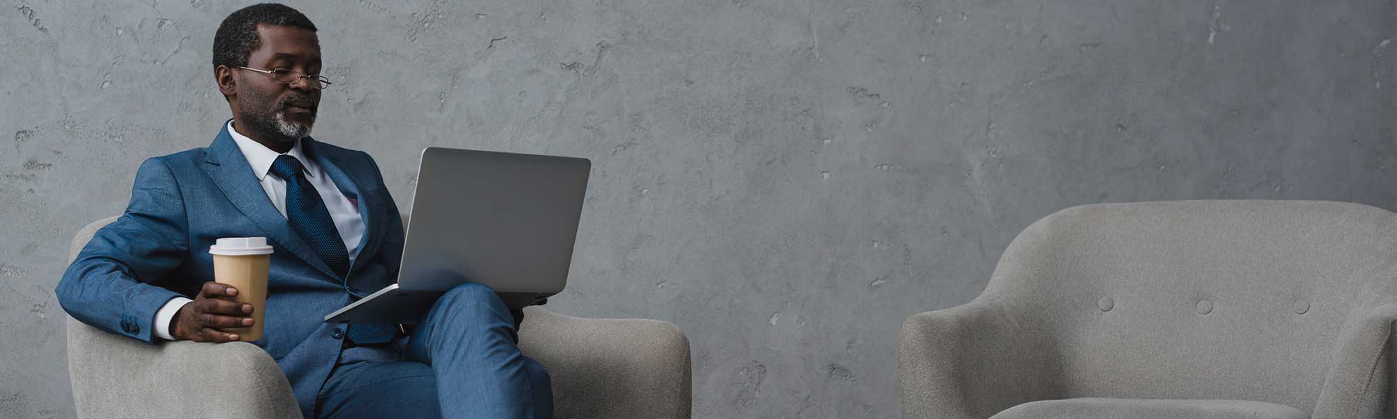 mature man sitting in chair with coffee and laptop