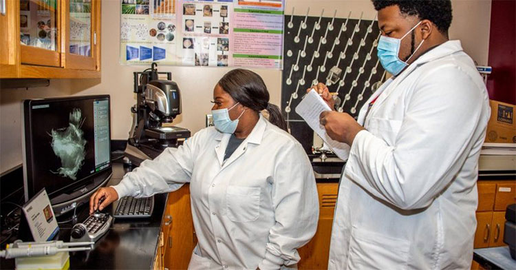 Students in lab coats reviewing monitor