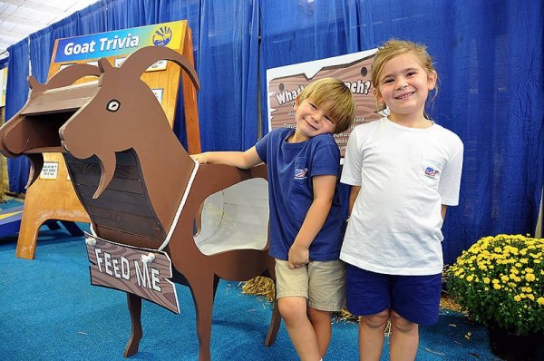 Two children standing next to a wooden goat.