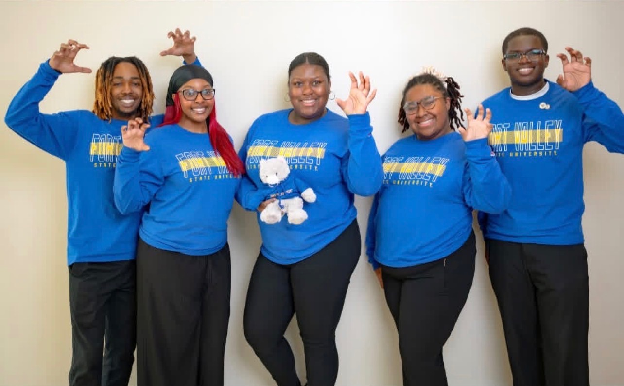 Group of people in blue shirts with hands raised in shape of Wildcat claw.