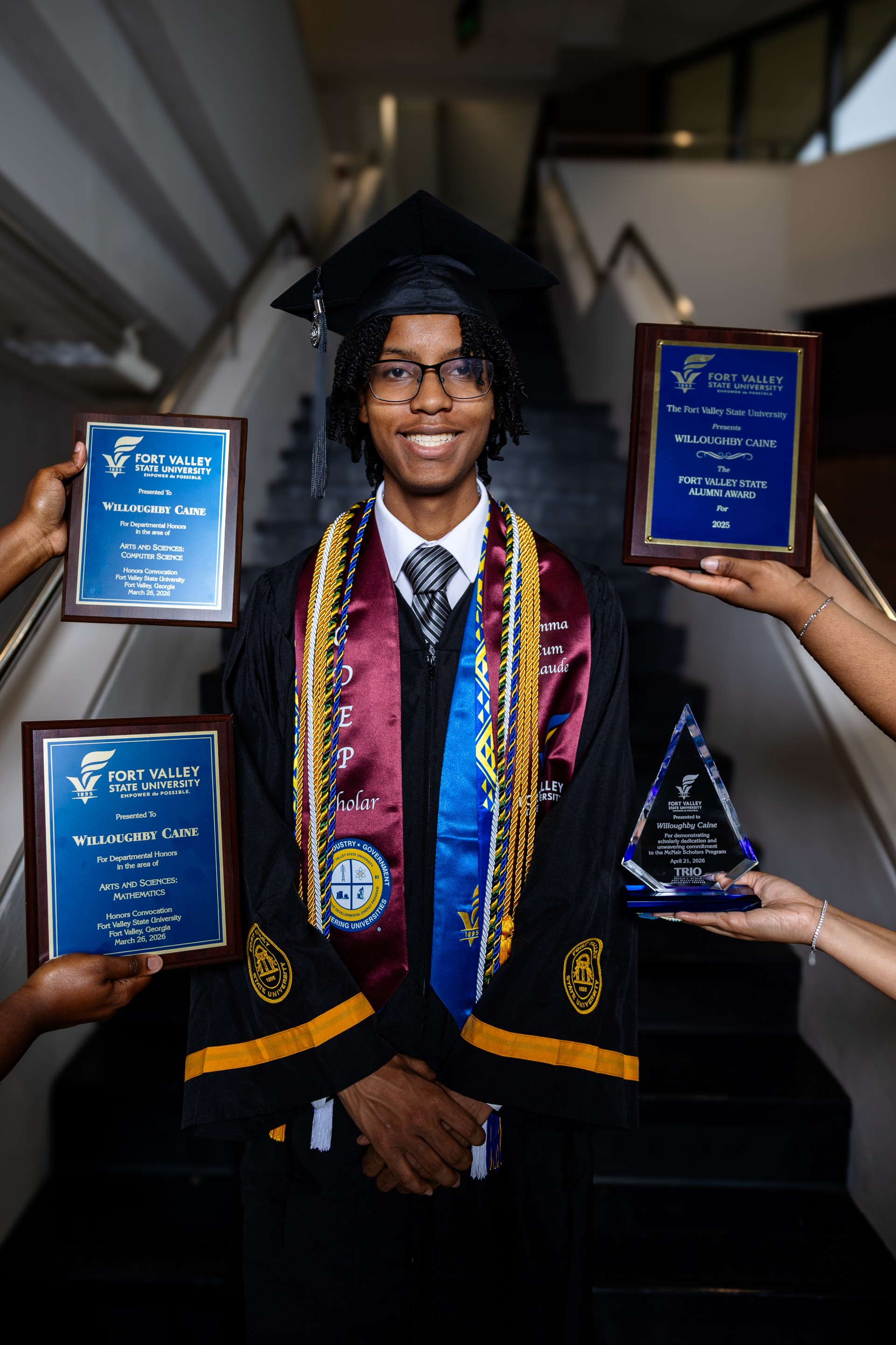 young man standing on steps with different people holding up awards next to him